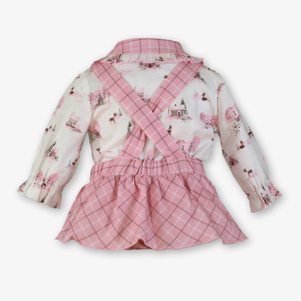 A baby girl's two-piece outfit featuring a long-sleeve collared shirt with a pink and white winter forest print, paired with matching pink plaid overalls with crisscross straps.
