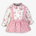 A baby girl's long-sleeve dress with a white and pink winter print on the top and a pink plaid skirt, shown on a light gray background.